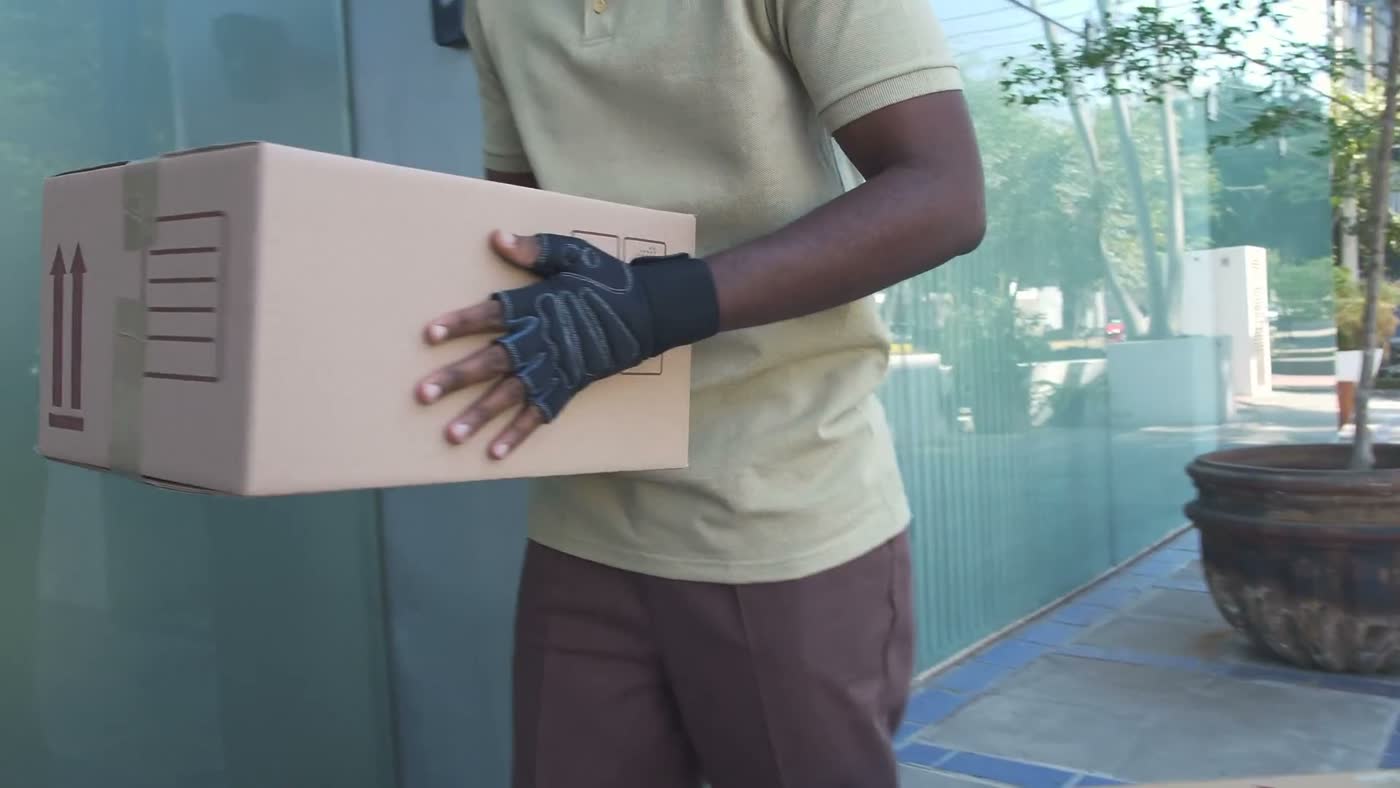 A crew member in work gloves carrying a box out of a building